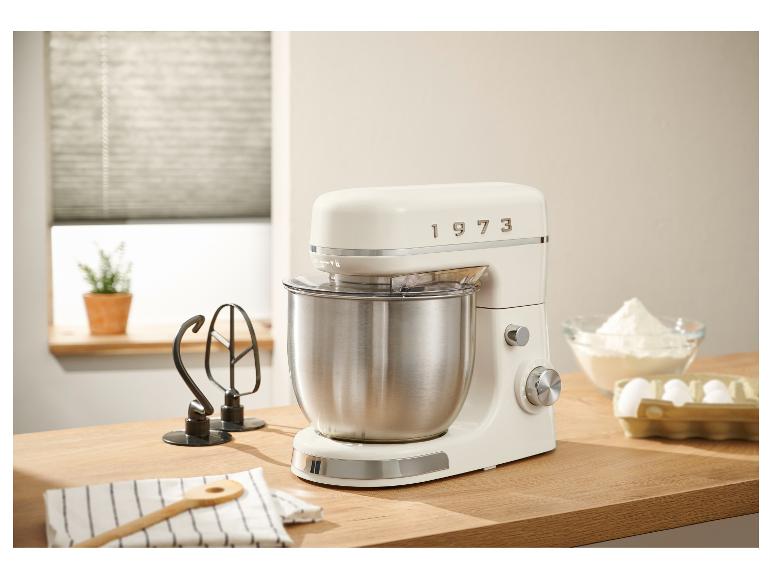 Un robot pâtissier crème style années 1973 sur un comptoir en bois, entouré d'ingrédients de pâtisserie.