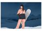 Femme en veste et pantalon de ski rose tenant un snowboard dans un paysage montagneux.