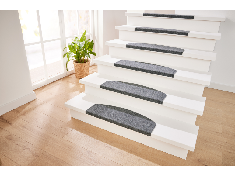 Escalier blanc avec tapis antidérapants gris, plante en pot et parquet clair.
