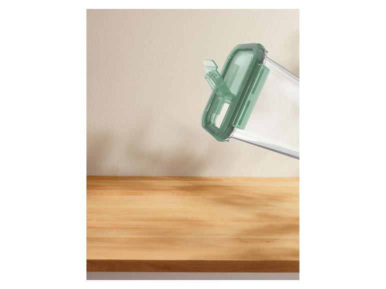 Récipient de conservation transparent avec couvercle vert, incliné au-dessus d'une surface en bois.