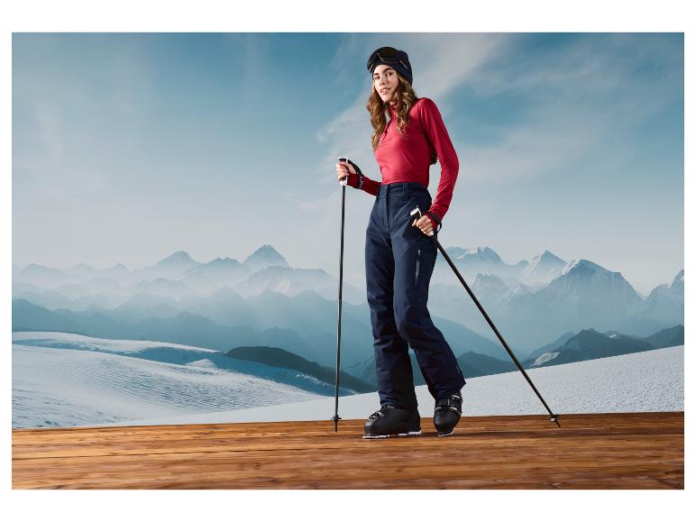 Une femme en tenue de ski avec des bâtons de ski se tient sur une plateforme en bois avec des montagnes en arrière-plan.