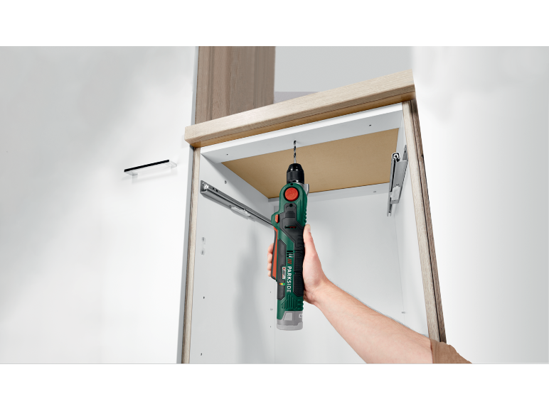 Une perceuse sans fil perçant une étagère en bois à l'intérieur d'une armoire.