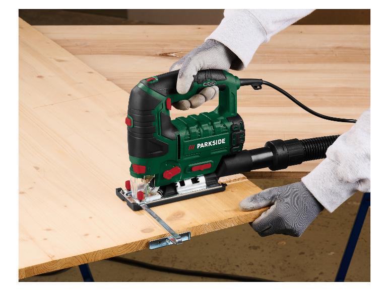 Une personne coupe une planche de bois avec une scie sauteuse électrique, portant des gants de protection.