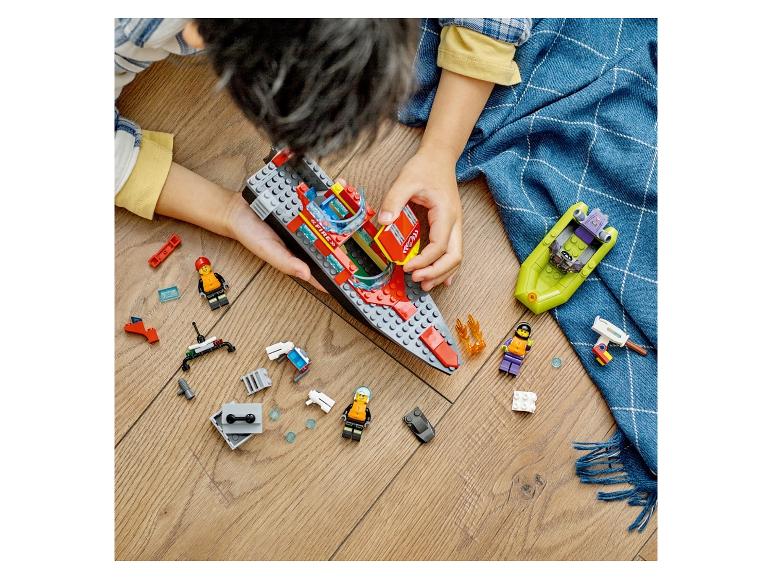 Enfant jouant avec des bateaux jouets et des figurines sur un plancher en bois.