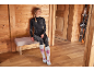 Femme en sous-vêtements thermiques et chaussettes de ski assise sur un banc dans une pièce en bois avec des skis.