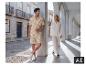 Homme en chemise et short beige à imprimé palmier, femme en ensemble de lin blanc, dans une allée voûtée.