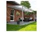 Pergola de terrasse grise avec toit transparent au-dessus d'un salon extérieur avec mobilier et plantes.