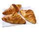 Trois croissants dorés sur une serviette blanche, prêts à être servis.