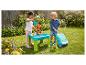 Deux enfants jouent avec une table à eau et à sable, une machine à bulles et un jouet à chevaucher dans un jardin.