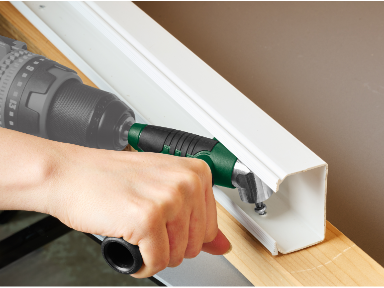 Personne utilisant une perceuse avec un adaptateur d'angle pour visser dans une goulotte blanche.