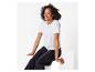 Femme souriante en T-shirt blanc et jean noir assise sur un bloc blanc.