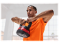 Un homme en t-shirt orange soulève un kettlebell.
