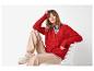 Femme en cardigan rouge, pantalon beige et baskets, assise sur une chaise blanche.