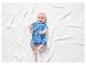 Un bébé allongé sur une couverture blanche avec un body bleu à imprimé dinosaure.