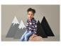 Une petite fille en veste bleue à motif d'ours et en jean assise sur une souche d'arbre.