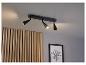 Un luminaire de plafond noir avec trois spots pointés sur un mur en bois.