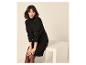 Femme en robe pull noire à col roulé et collants, assise sur un banc blanc.
