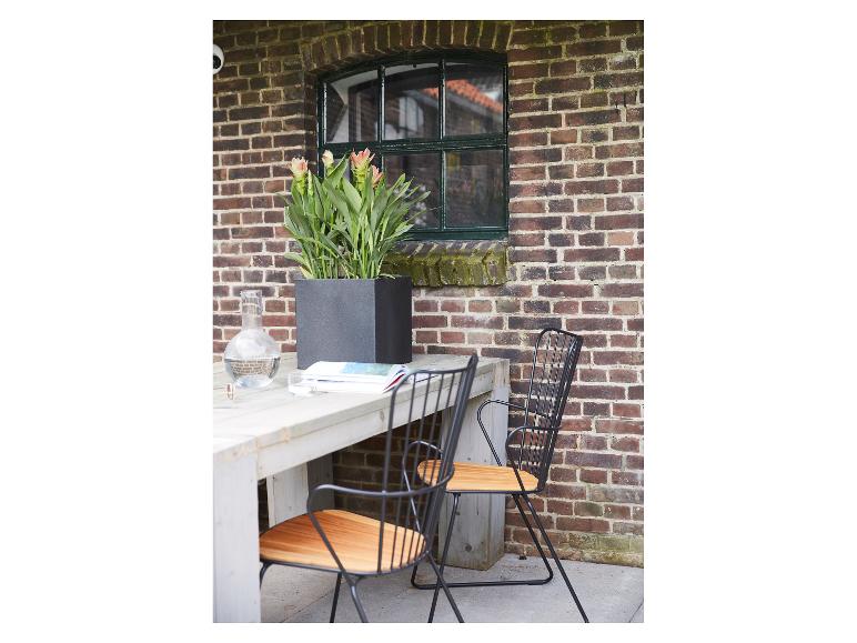 Table de jardin avec chaises, jardinière de fleurs et carafe devant un mur de briques.