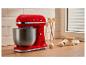 Robot pâtissier rouge avec bol en acier inoxydable, œufs et farine sur un comptoir en bois.