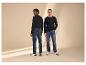 Deux hommes en hauts à manches longues et jeans, l'un regardant en arrière, l'autre souriant.