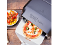 Four à pizza avec pizza fraîche sur une pelle, à côté de tomates cerises.
