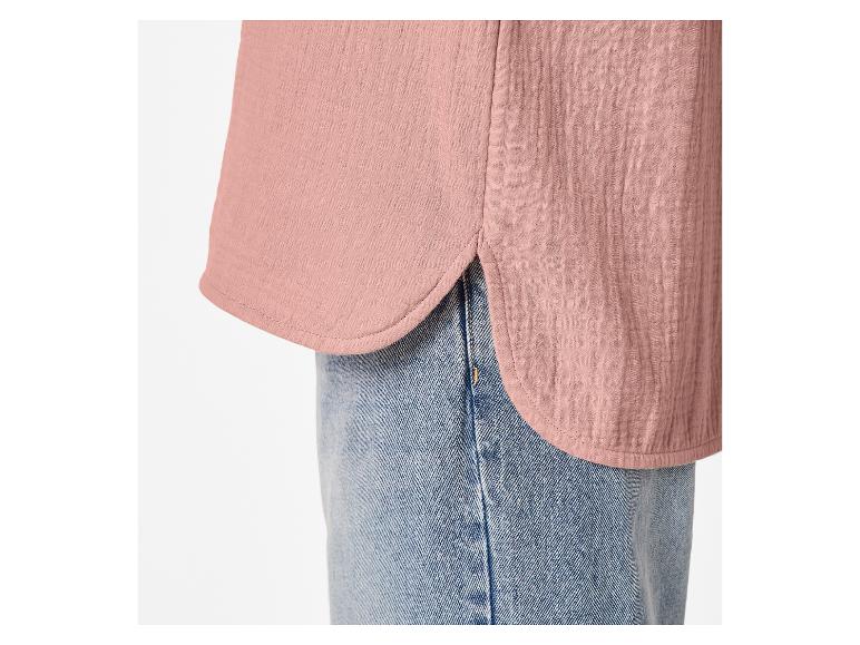 Détail d'une chemise en mousseline rose avec ourlet arrondi et jean bleu.