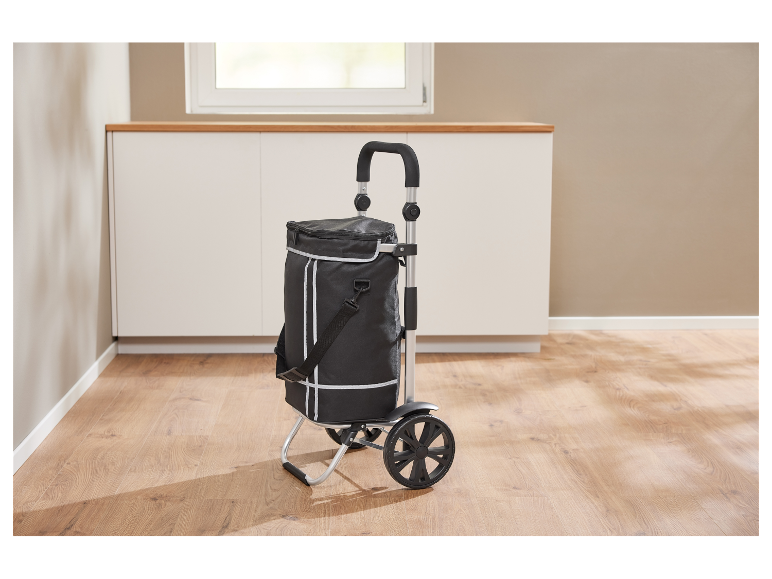 Un chariot de courses pliable noir avec fonction de refroidissement se trouve sur un sol en bois.