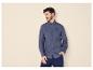 Homme en chemise bleue à manches longues et pantalon bleu, une main dans la poche.