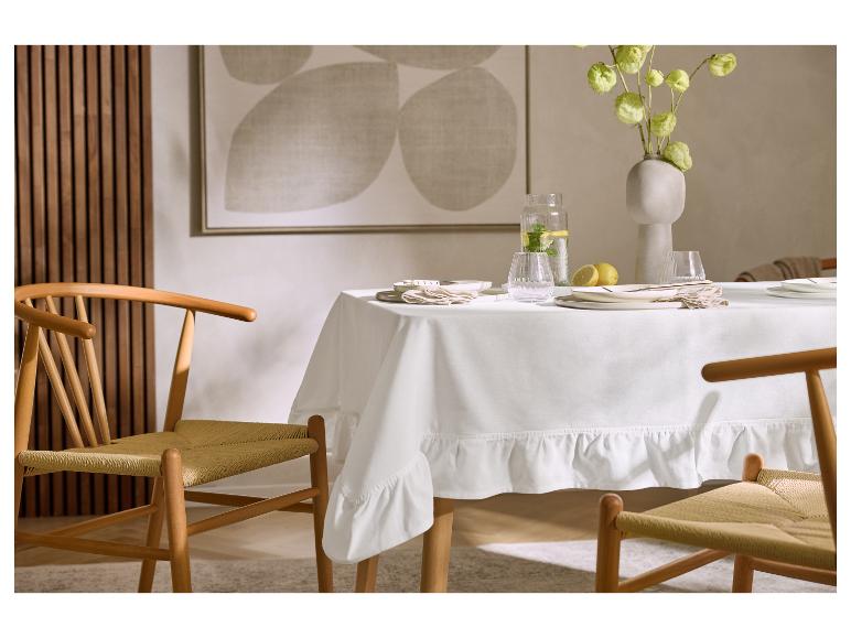 Table à manger avec nappe blanche, vaisselle, vase de fleurs et chaises en bois.