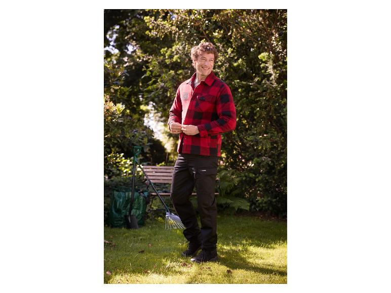 Homme dans le jardin en pantalon de travail noir PARKSIDE® et chemise rouge.