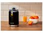Presse-agrumes noir avec un verre de jus et des oranges sur une table en bois.