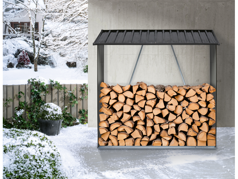 Bois de chauffage empilé dans un range-bûches noir, avec un paysage hivernal enneigé en arrière-plan.