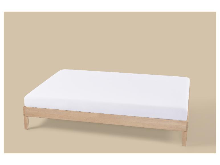 Lit en bois clair avec matelas blanc sur fond beige.