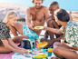 Un groupe de personnes profite d'un pique-nique sur la plage avec une glacière et de la vaisselle colorée.