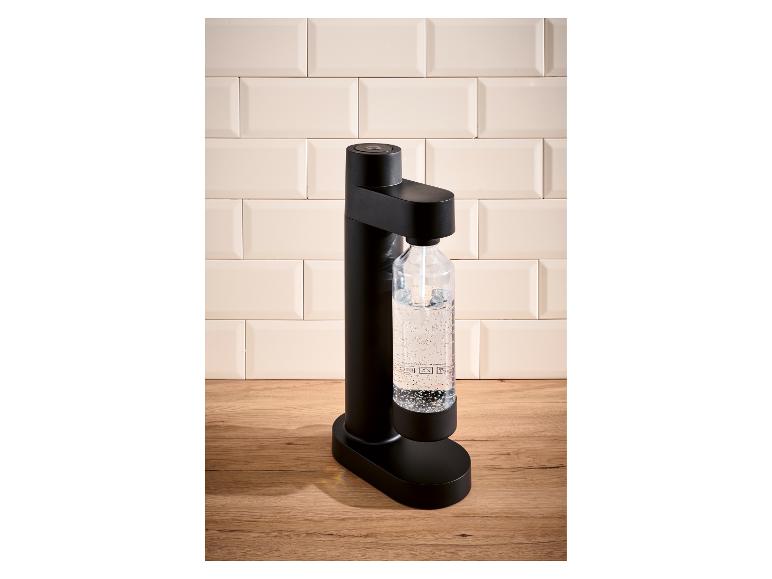 Machine à eau pétillante noire avec une bouteille d'eau gazéifiée sur un comptoir en bois