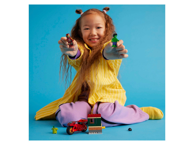 Une fille tient des figurines Lego d'Iron Man et de Hulk.
