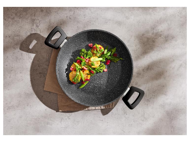 Poêle à frire avec des légumes sautés colorés sur un fond en béton.
