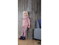 Fille souriante en pull tricoté rose et pantalon, appuyée contre un mur en bois.