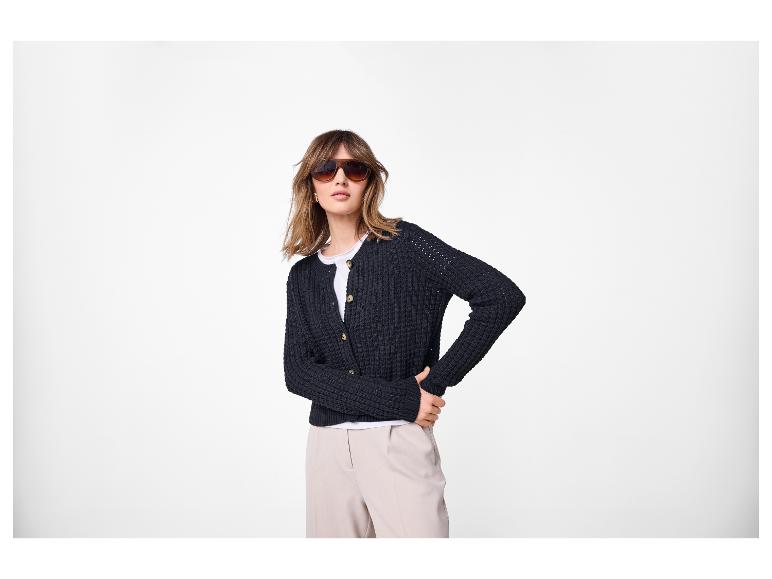 Femme en cardigan noir, t-shirt blanc et pantalon beige, portant des lunettes de soleil