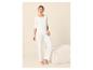 Femme en pyjama blanc à manches longues et pantalon, posant à côté d'un pouf crème.