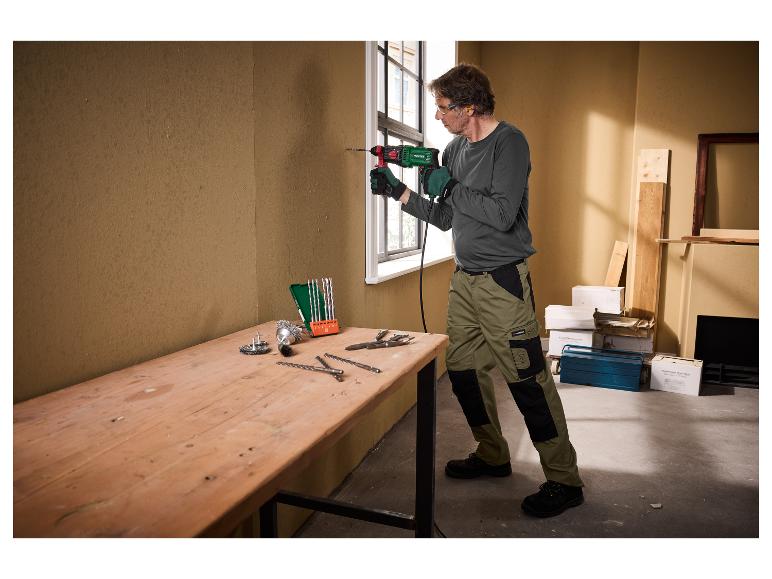 Homme avec des gants et des lunettes de sécurité perçant un mur avec une perceuse Parkside.