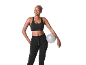 Femme souriante en tenue de sport noire, tenant un petit ballon de fitness gris.