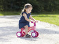 Une petite fille roule sur une draisienne rose avec des roues blanches.