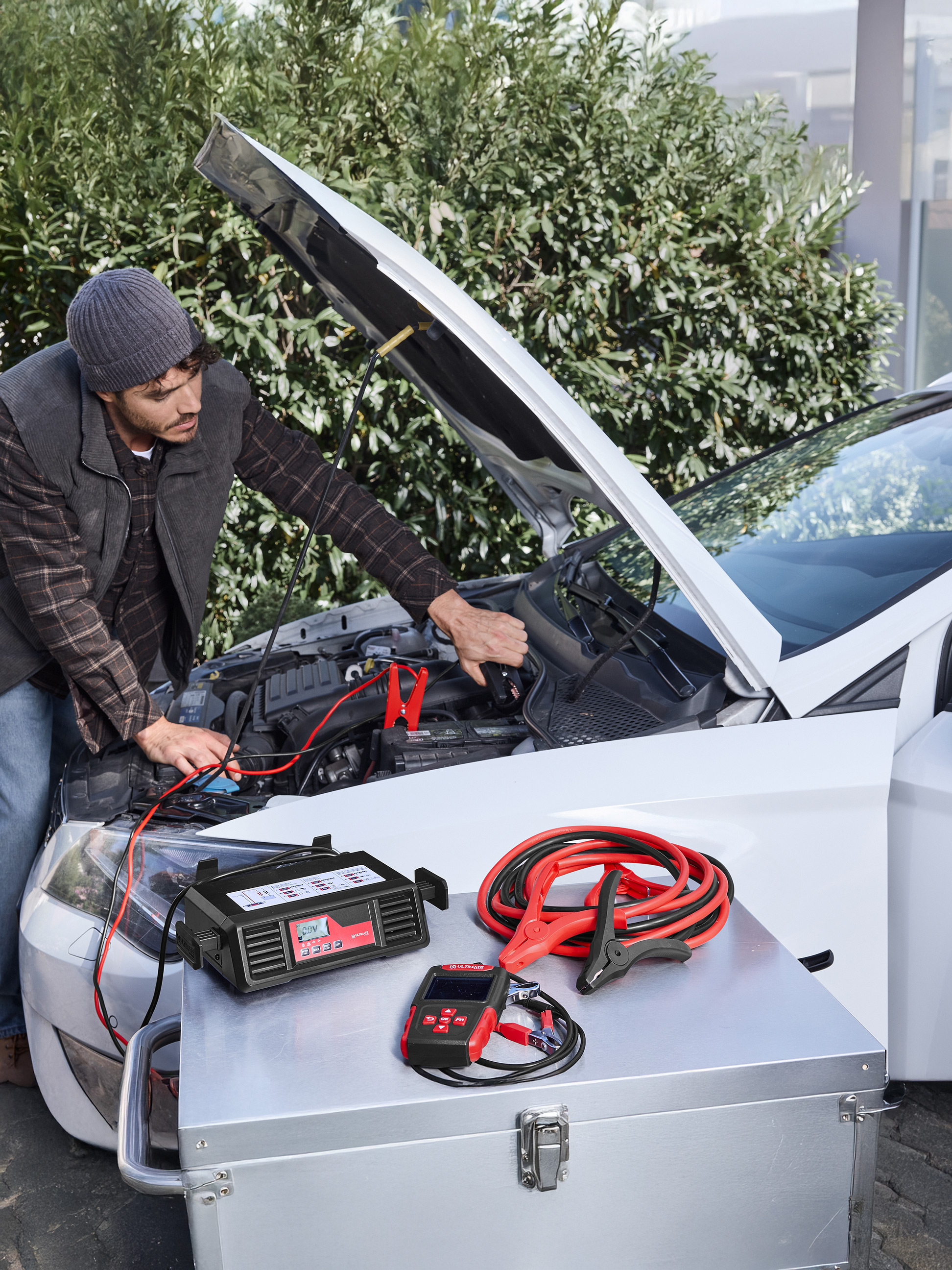 Homme utilisant un chargeur de voiture ULTIMATE SPEED et des câbles de démarrage sur une voiture.