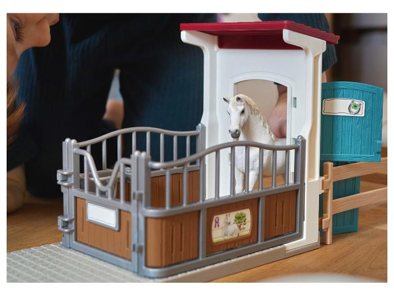 Enfant jouant avec une écurie jouet avec un cheval blanc.