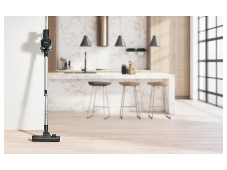 Aspirateur balai noir et argent dans une cuisine moderne avec îlot et tabourets de bar.