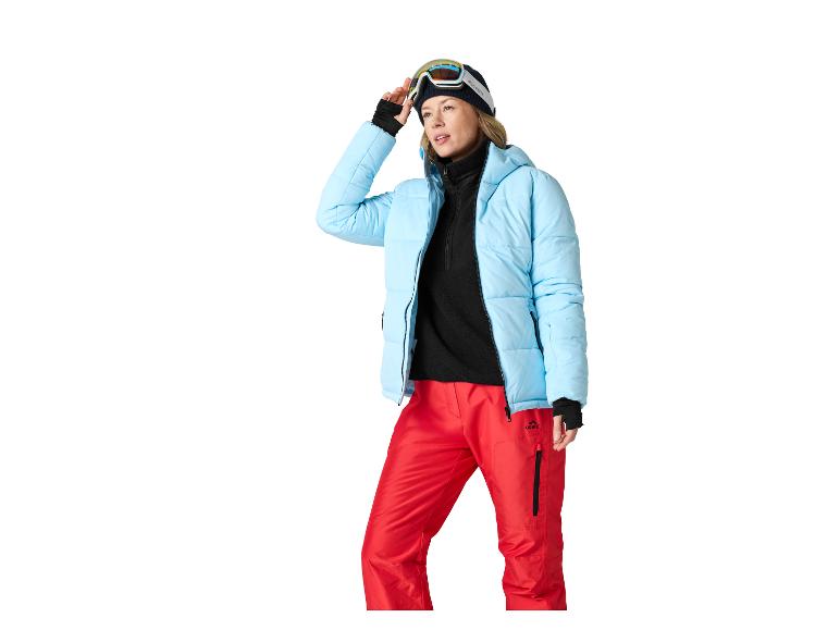 Femme en veste de ski bleue, pantalon rouge et lunettes de ski.