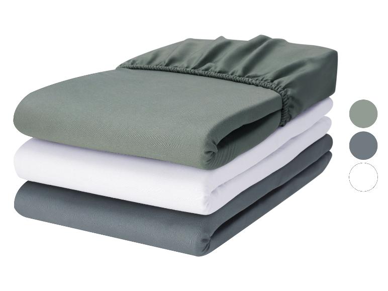 Pile de trois draps-housses pliés en vert, blanc et gris.
