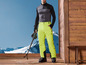 Un homme en tenue de ski se tient debout sur une plate-forme en bois avec des skis.