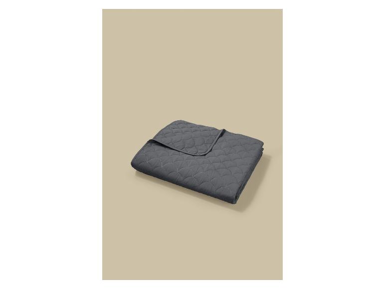 Couverture matelassée gris foncé avec un motif en écailles, pliée sur un fond beige.